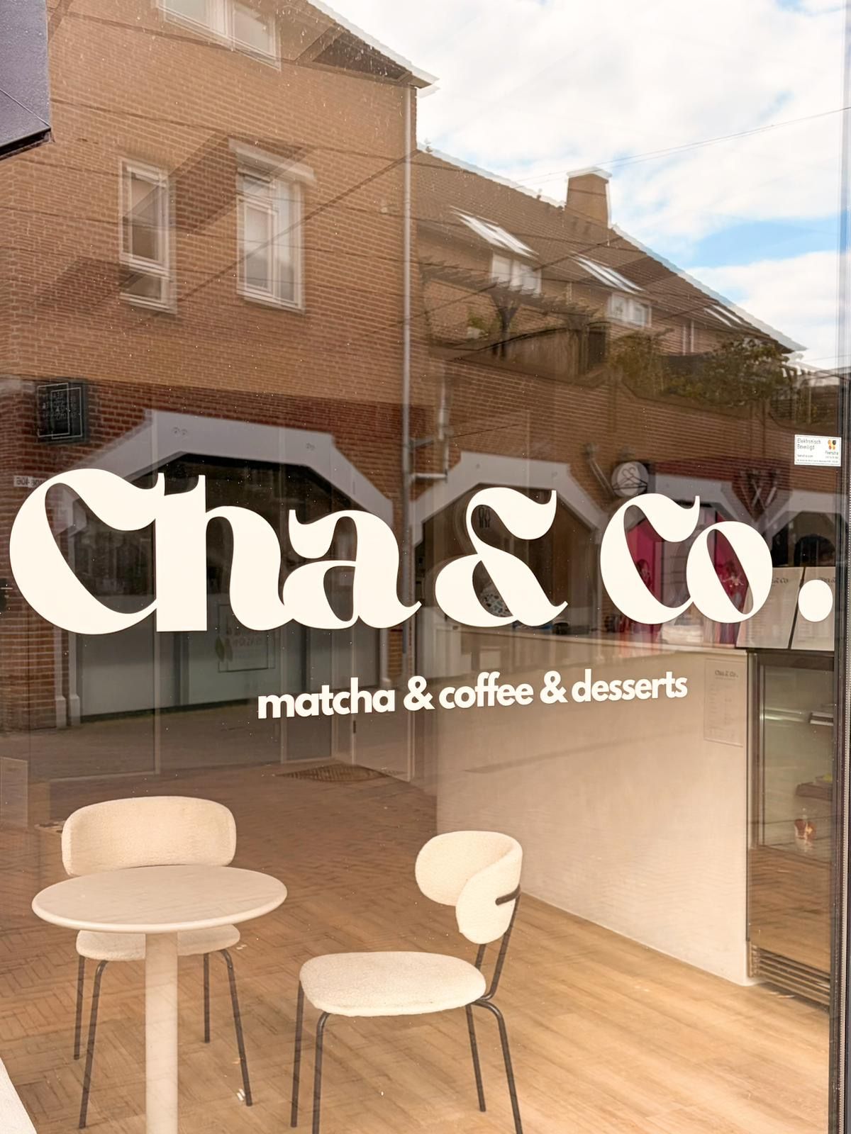 De etalage van Cha & Co. met de witte belettering matcha & coffee & desserts en de ronde tafeltjes binnen