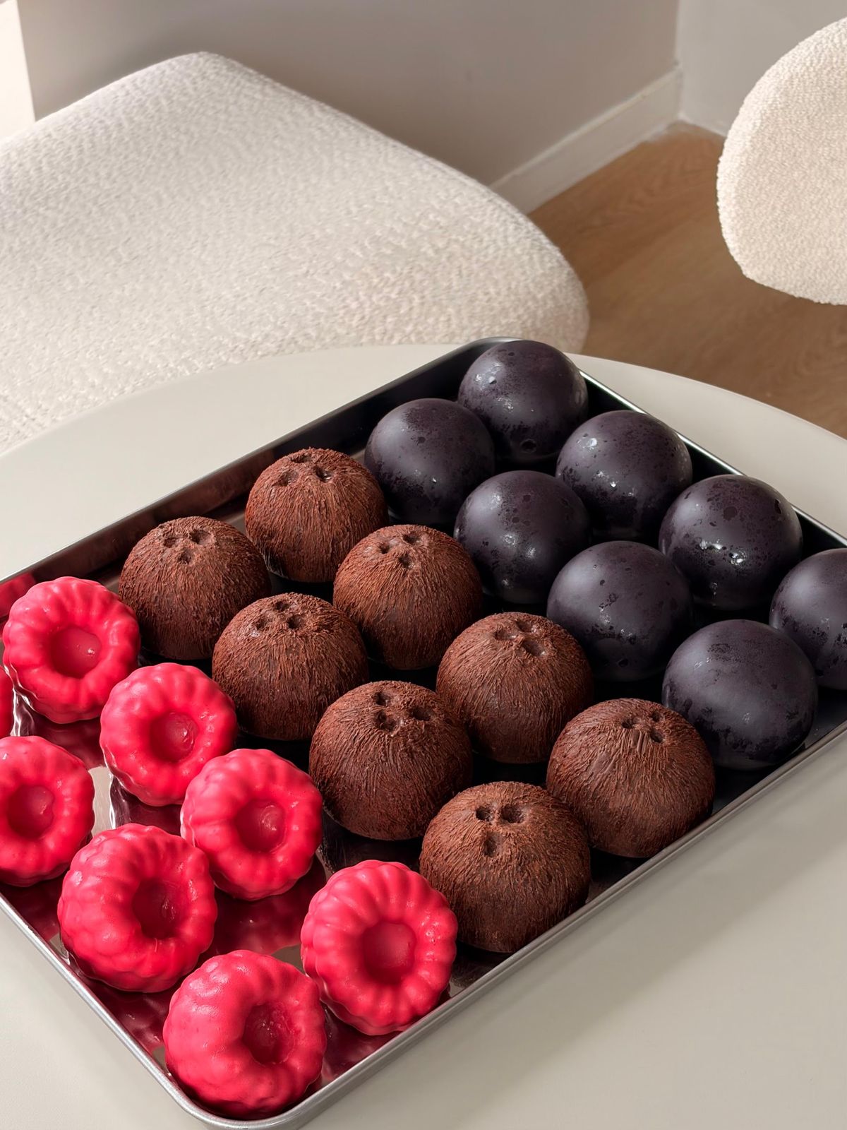 Een bakplaat vol desserts in de vorm van frambozen, kokosnoten en pruimen
