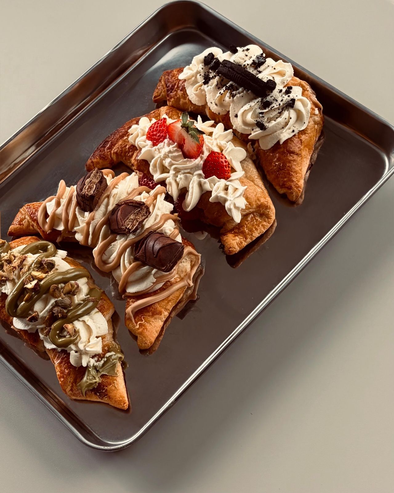 Een bakplaat met croissants gevuld met slagroom, aardbeien, Oreo en chocolade