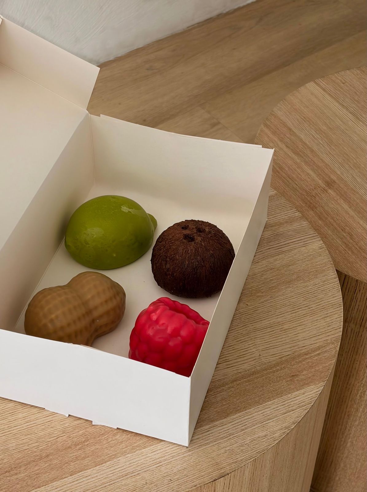 Een geopend wit doosje met vier fruitdesserts: limoen, kokos, pinda en framboos