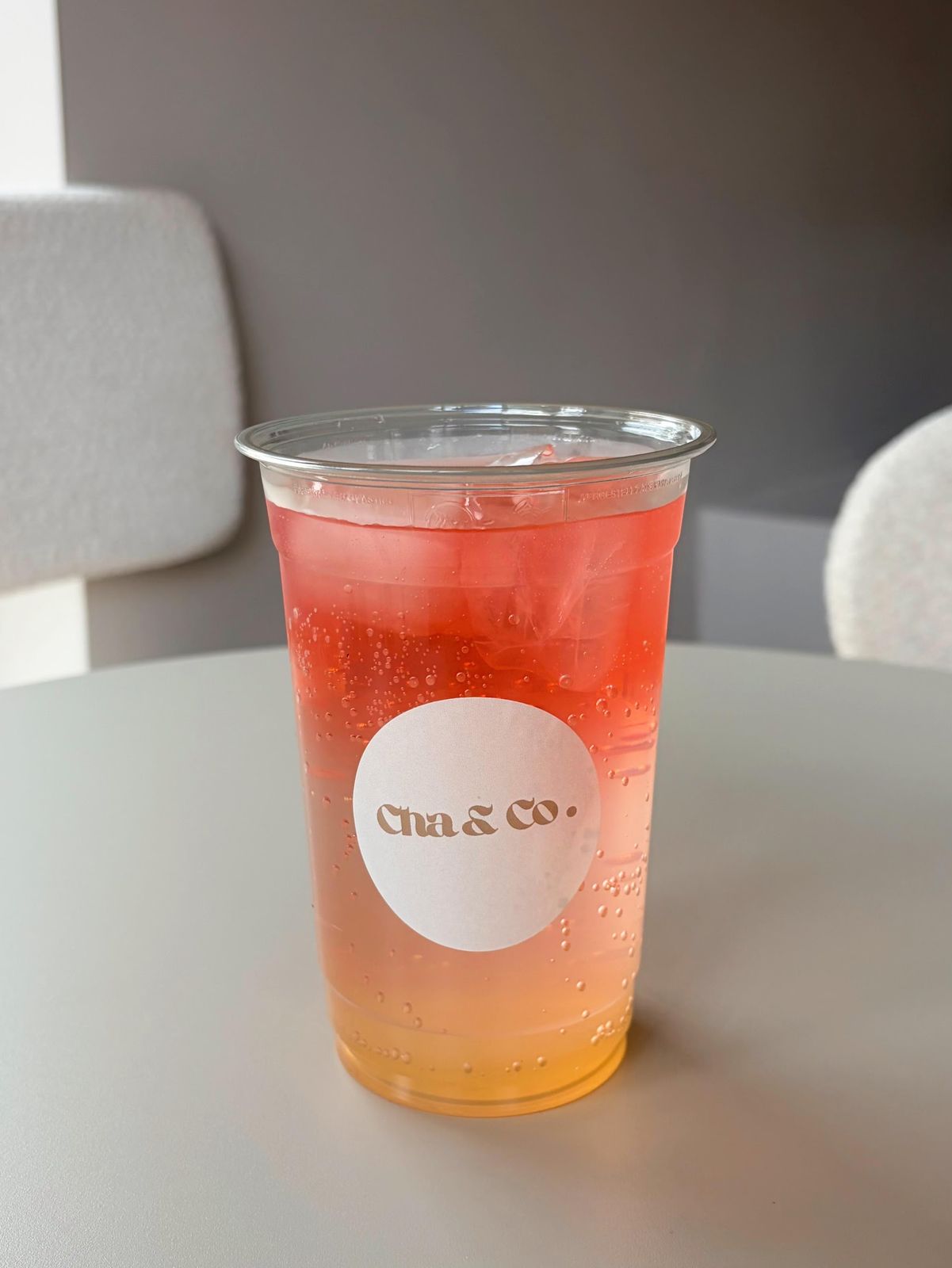 Rood-oranje ijsdrankje met bubbels in een beker met het Cha & Co. etiket